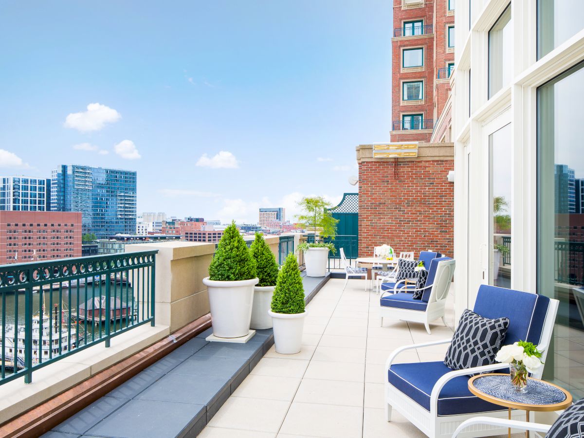 A modern rooftop terrace with potted plants, cushioned seating, and a city skyline in the background on a bright day, ending the sentence.